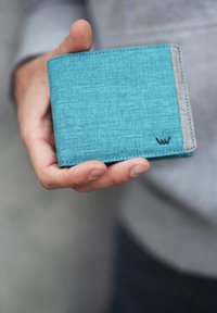 Blue fabric wallet with a textured finish, gray accent, and small logo detail. Held in a hand, showcasing its compact design.