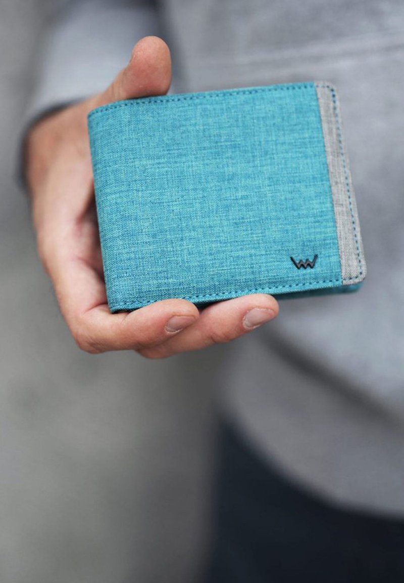 Blue fabric wallet with a textured finish, gray accent, and small logo detail. Held in a hand, showcasing its compact design.