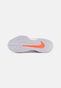 Sohle eines weißen Sportschuhs mit Zickzack-Profil und leuchtend orangefarbenem Nike-Swoosh-Logo auf einem schlichten weißen Hintergrund.