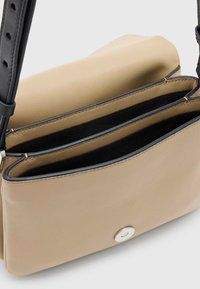 Borsa a tracolla in pelle beige con forma rettangolare, dotata di una tracolla nera e due scomparti interni foderati in tessuto nero. Dettaglio della chiusura in argento.