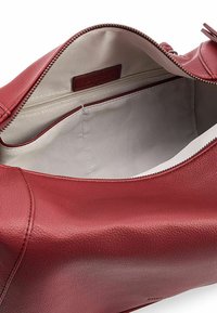 Bolso de cuero rojo con una textura lisa y granulada, que cuenta con un cierre de cremallera y un interior de tela de color claro con un bolsillo adicional con cremallera.