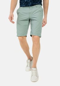 Hellgrüne Shorts aus einem glatten Baumwollmix, mit umgeschlagenen Säumen, seitlichen Taschen und flachem Bund. Getragen mit weißen Sneakers.
