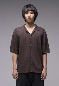 Πουκάμισο με κοντά μανίκια και κουμπιά, σε καφέ χρώμα, με πλεκτή υφή, γιακά και άνετη εφαρμογή.