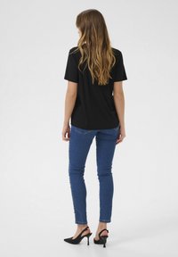 Maglietta nera a maniche corte, abbinata a jeans blu slim e tacchi a punta neri; tessuto morbido con una vestibilità comoda.