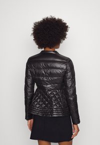 Czarna pikowana kurtka puchowa o dopasowanym kroju, z poziomymi i diamentowymi wzorami, długimi rękawami i kołnierzem.