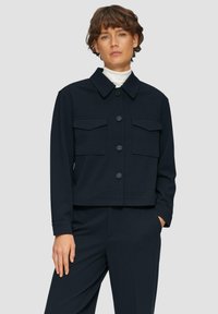 Marineblauwe cropped jacket van zacht materiaal met een knoopsluiting aan de voorkant, twee borstzakken en een klassieke kraag.
