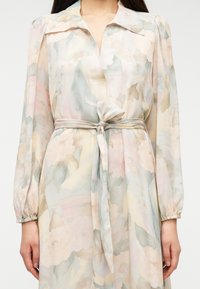 Μακρύ, διάφανο φλοράλ φόρεμα με απαλούς παστέλ χρωματισμούς, με ζώνη δέσιμο στη μέση και φουσκωτά μανίκια, με απαλή υφή υφάσματος.