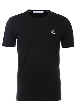 T-shirt noir à manches courtes avec col rond, petit logo blanc "cK" sur le côté gauche de la poitrine et étiquette "Calvin Klein Jeans" à l'intérieur du col.