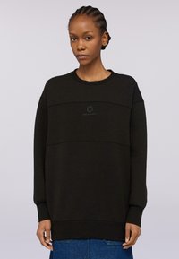 Svart oversized sweatshirt i mjukt material med rund halsringning, med en tonad logotyp centrerad på bröstet och ribbade muddar.