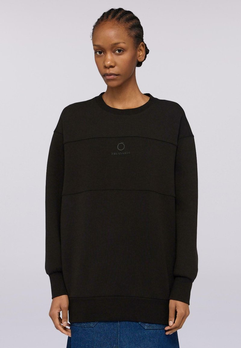 Svart oversized sweatshirt i mjukt material med rund halsringning, med en tonad logotyp centrerad på bröstet och ribbade muddar.