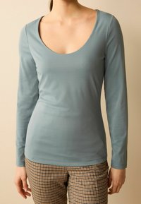 Maglia a maniche lunghe in morbido tessuto azzurro chiaro con scollatura tonda, abbinata a pantaloni a quadretti marroni con un motivo a scacchi.