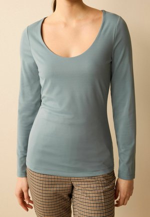 Haut à manches longues en tissu doux et bleu clair, avec un décolleté en forme de U, associé à un pantalon à carreaux marron présentant un motif à damier.