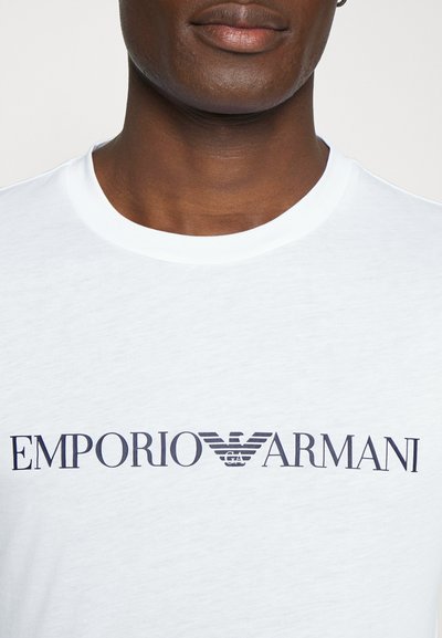 Hvit bomulls t-skjorte med en blå "EMPORIO ARMANI" logo med vingedetaljer. Rund hals design med korte ermer og jevn tekstur.