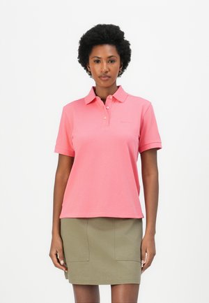 Roze polo shirt met een klassieke kraag, korte mouwen en een relaxte pasvorm. Gecombineerd met een groene rok met twee voorzakken.
