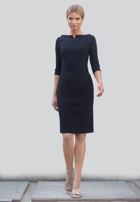 Granatowa dopasowana sukienka z rękawami o długości trzech ćwierć, z dekoltem okrągłym, w połączeniu z cielistymi rajstopami w siatkę i beżowymi sandałami na słupku.
