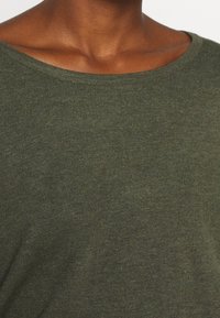 Olivgrön stickad topp med båthals. Tyget har en fin textur och lätt stretch, vilket ger en bekväm passform.