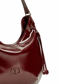 Borsa hobo in pelle bordeaux con finitura lucida, dotata di tracolla rimovibile e di un accento con logo. Texture liscia e forma arrotondata.
