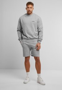 Grijze sweatshirt met een ronde hals en logo, gecombineerd met grijze shorts. Beide items hebben een zachte, comfortabele textuur. Witte sneakers ronden de look af.