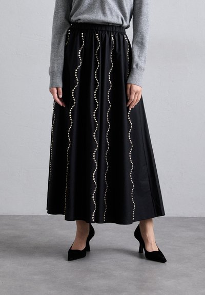 Jupe maxi noire avec une taille élastique, présentant un motif ondulé de clous décoratifs. Fabriquée en tissu lisse, principalement unie sans accents supplémentaires.