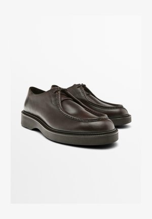 Brown leather shoes with a rounded design, stitched detailing along the upper, and a thick rubber sole. Features laces for secure fit.