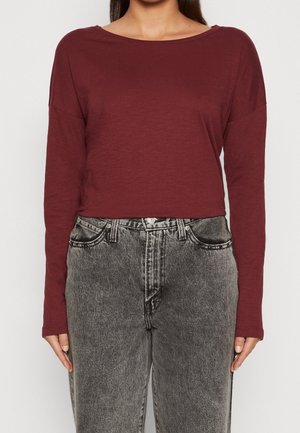 Top lungo bordeaux a maniche lunghe con vestibilità ampia; scollatura a girocollo. Abbinato a jeans in denim neri sbiaditi a vita alta con tasche anteriori.