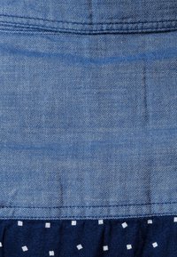 Tessuto in denim blu con una texture liscia, caratterizzato da un fondo arricciato blu navy decorato con motivi quadrati bianchi.