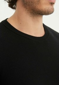 Pull en maille noir avec un col rond et un tissu texturé, montrant les détails du col et évoquant un matériau doux et respirant.