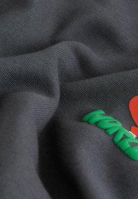 Szary materiał o miękkiej teksturze, z czerwonym sercem i zielonym napisem. Materiał ma prążkowany wzór i gładką powierzchnię.