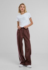 Hvit t-skjorte med "DELILICIOUS" i sølvbokstaver, kombinert med brune sateng joggere med rosa sidestrek og elastisk midje.