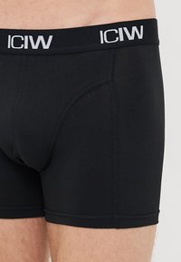 Boxer briefs neri da uomo con logo bianco "ICIW" sulla cintura, indossati da una persona che mostra la parte superiore della coscia e la zona della vita.