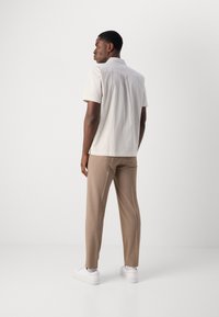Camisa de color claro de manga corta con patrón texturizado, combinada con pantalones beige y zapatillas blancas. Vista desde la parte trasera.