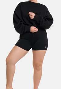 Černý oversized svetr v kombinaci s černými žebrovanými šortkami. Látka je hladká s minimální strukturou, na šortkách se nachází malé logo.