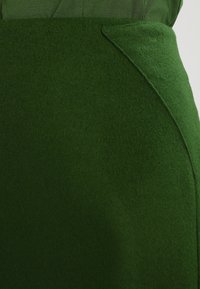 Falda de lana verde con textura suave, diseño ajustado y detalle de costura lateral para una apariencia refinada.