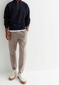Sudadera navy con cremallera, pantalones grises claros ajustados con costuras laterales y zapatillas blancas con acentos beige. Diseño y ajuste minimalista.