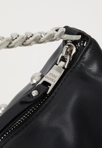 Sac à main en simili cuir noir avec une bandoulière en chaîne argentée, fermeture éclair et accents métalliques, y compris un logo en relief et des rivets.