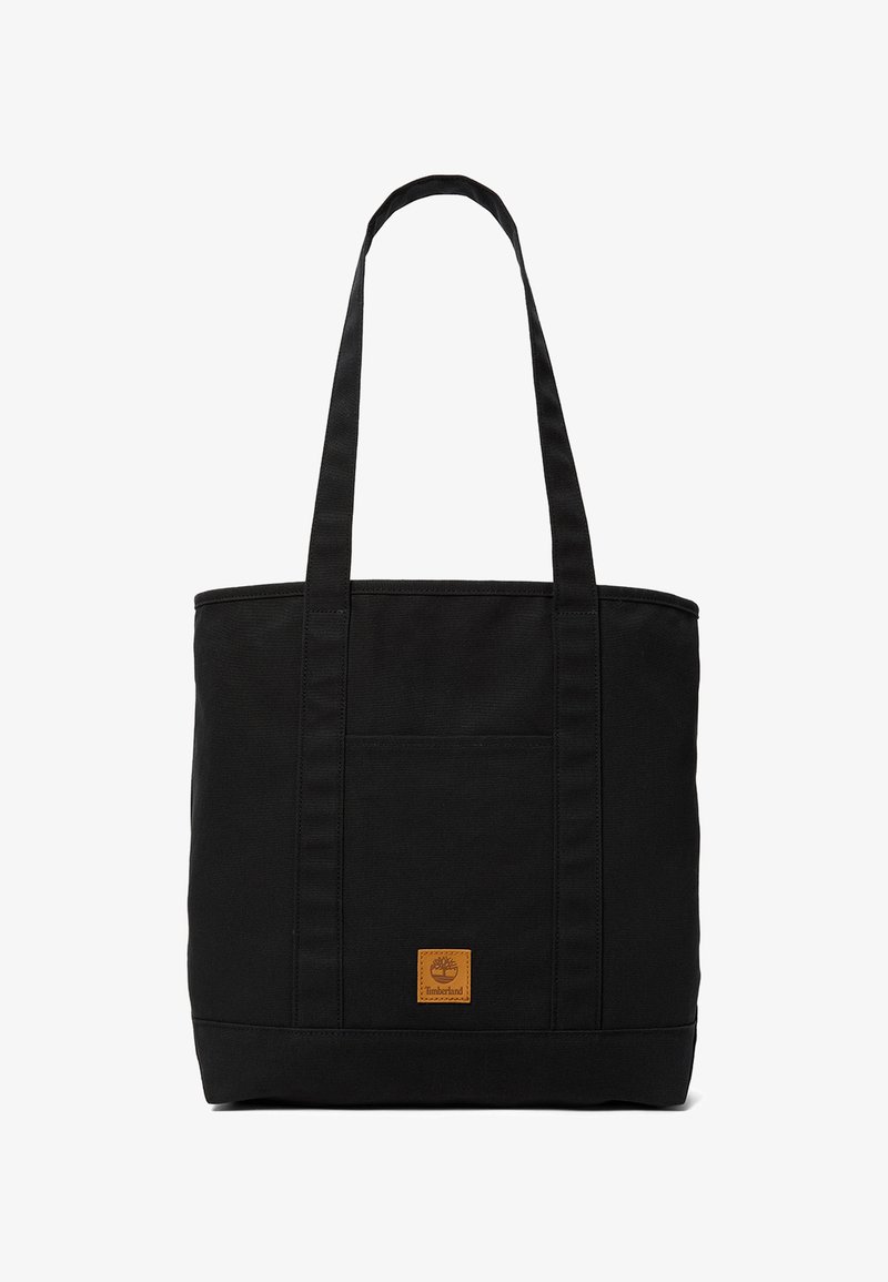 Black canvas tote bag with long handles and a small brown Timberland logo patch centered near the bottom.