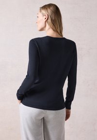 Námořnická modrá košile s dlouhými rukávy, kulatým výstřihem a přiléhavým střihem, doplněná o šedé, volné tepláky. Měkká textura, minimální detaily.