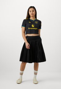Crna kratka majica od jerseya s žutim i plavim akcentima, na kojoj se nalazi logo "Snapdragon". Uparena s crnom suknjom s plisiranjem i tenisicama s uzorkom.