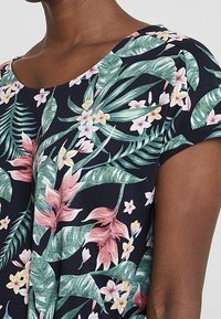 Top w kwiecisty wzór na granatowym tle, z krótkimi rękawami i okrągłym dekoltem, z intensywnymi różowymi, zielonymi i białymi akcentami kwiatowymi.