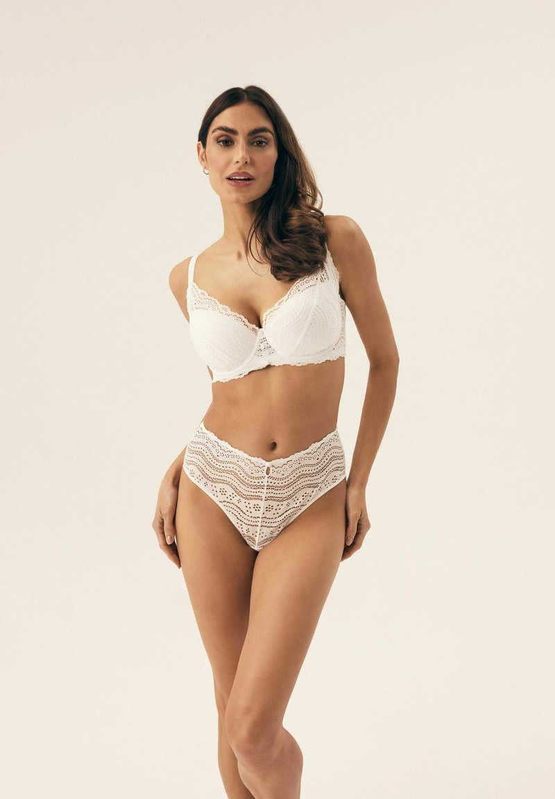 Biała koronkowa bielizna składająca się z usztywnionego biustonosza z falbankami oraz majtek o wysokim stanie z poziomymi wycięciami.