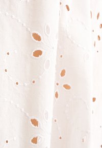 Tessuto di cotone bianco con ricami floreali intricati e motivi a intaglio, dalla texture liscia e dal drappeggio morbido.