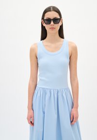 Haut sans manches côtelé bleu clair associé à une jupe fluide bleu clair, avec une taille froncée et une texture lisse. Lunettes de soleil en forme de chat noires.