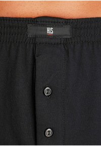 Melni kokvilnas šorti ar teksturētu jostasvīru, centrālā pogu rinda ar divām melnām pogām un uzšūtu birku pie jostas.