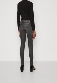 Jeans de denim gris ajustados con un acabado descolorido, con bolsillos traseros y una cintura de media altura, combinados con botas negras de tacón puntiagudo.