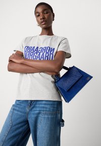 Gray t-shirt with large blue text, blue bag with a flap, and denim jeans featuring side pockets and a relaxed fit.