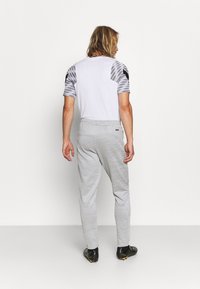 Witte T-shirt met grijze patroonmouwen, gecombineerd met lichtgrijze sweatpants. De broek heeft een zachte textuur en een elastische tailleband.