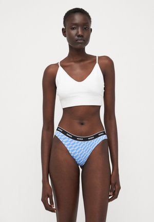 Witte bralette met dunne bandjes, gecombineerd met een blauwe thong met een herhalend wit "HUGO" logo op de tailleband en een gladde textuur.
