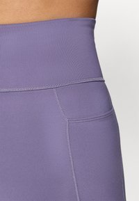 Højtaljede lilla leggings lavet af glat, strækbart stof, med kontrasterende syninger og en slank pasform.