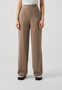 Wide-leg pants in a light brown fabric with a smooth texture. High waist design, paired with shiny silver platform shoes.