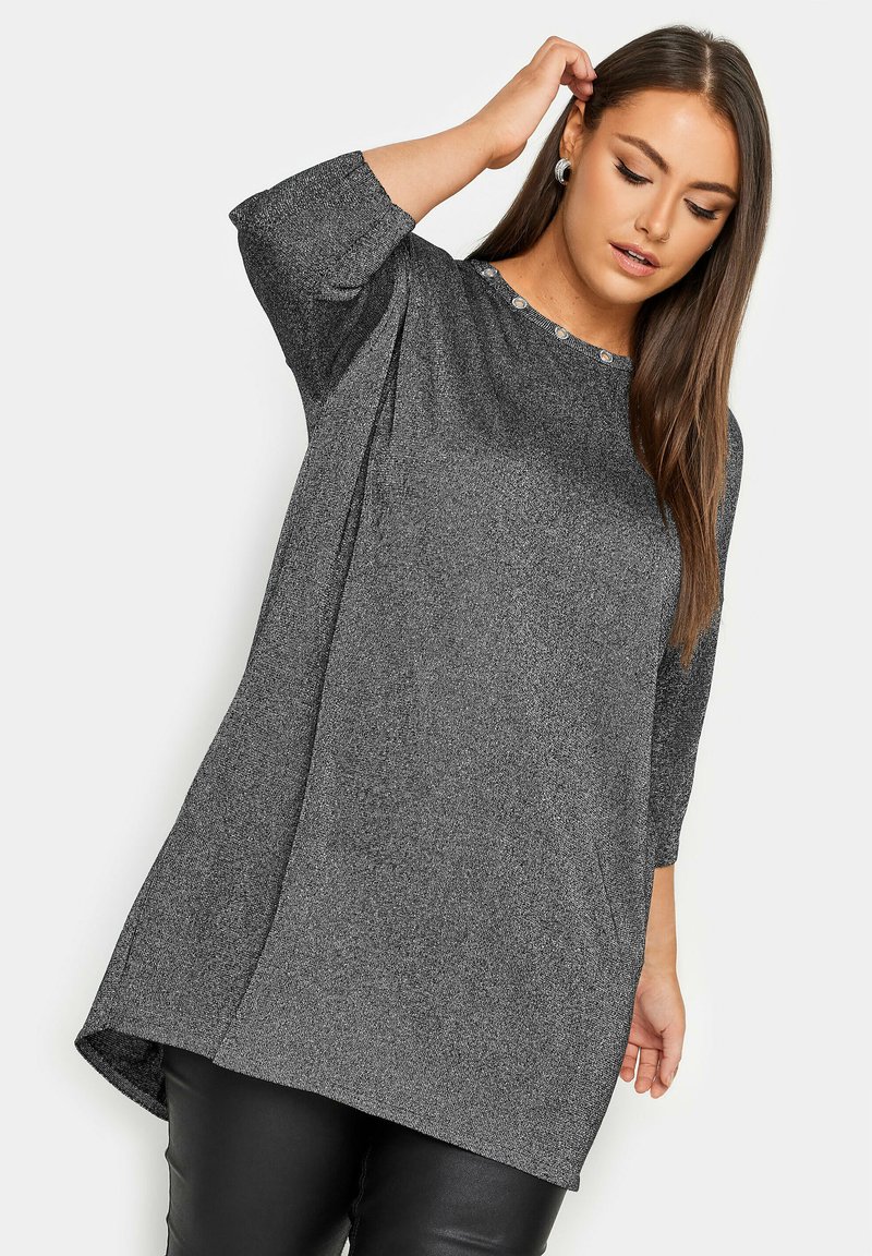Graue, lässige Tunika mit Dreiviertelärmeln, Rundhalsausschnitt und Knopfdetails; der Stoff hat eine weiche, strukturierte Oberfläche.